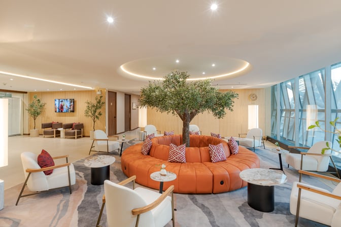The Coral Finest Business Class Lounge Cocoon at Suvarnabhumi Airport features circular seating with tables and a central decorative tree.
