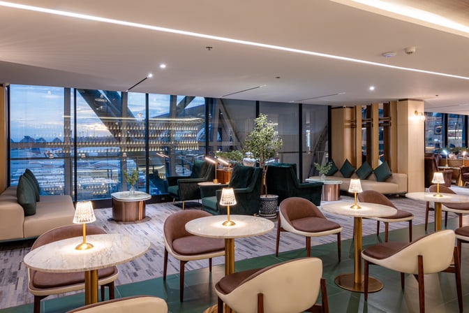 The Coral Finest Business Class Lounge at Suvarnabhumi Airport features seating with tables and views of the airport through large windows.