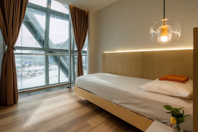 A private resting area in The Coral Finest Business Class Lounge at Suvarnabhumi Airport features a bed and large window with tarmac views.
