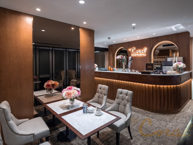 The Coral First Class Lounge at Suvarnabhumi Airport features a bar with complimentary beverages and a seating area with tables.
