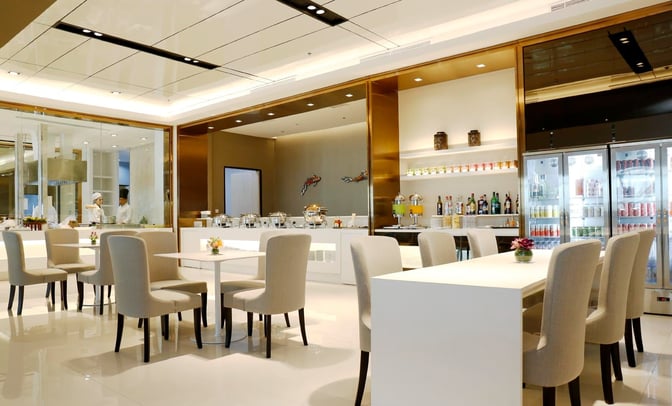 The Miracle Business Class Lounge at Suvarnabhumi Airport features a dining area with table seating and a self-serve beverage station.