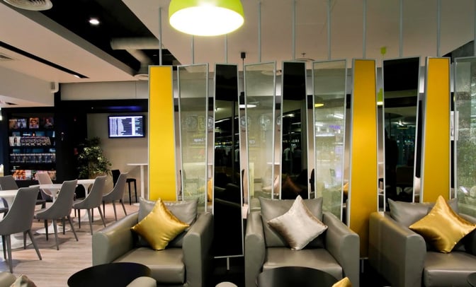 Comfortable seating in the Miracle Business Class Lounge at Suvarnabhumi Airport includes armchairs with small tables and a view of the flight information screen.