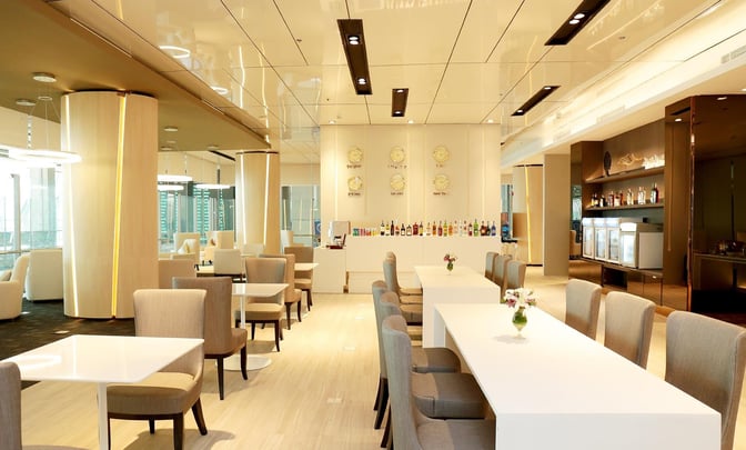 The Miracle First Class Lounge at Suvarnabhumi Airport features a seating area with tables and chairs, and a bar offering various beverages.