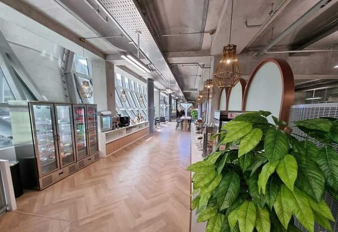 Self-serve beverage and snack area at Miracle Lounge, Suvarnabhumi Airport, featuring refrigerated drinks and coffee machines along a counter.