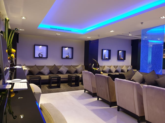 The Oman Air First and Business Class Lounge at Suvarnabhumi Airport features comfortable seating with workstations and decorative wall displays.