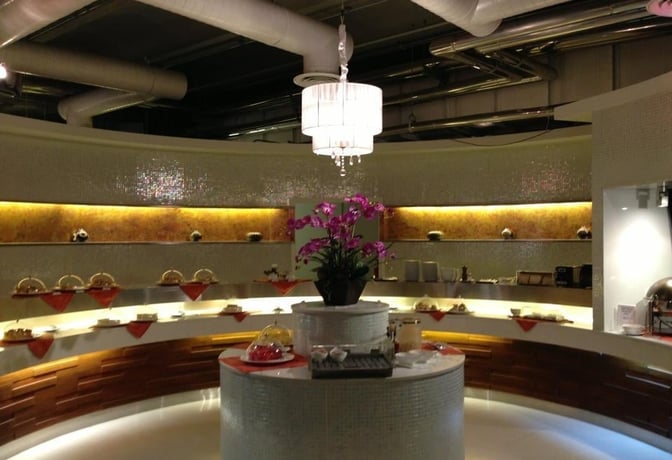 The Miracle First Class Lounge at Suvarnabhumi Airport features a circular buffet area with covered dishes and a central floral display.