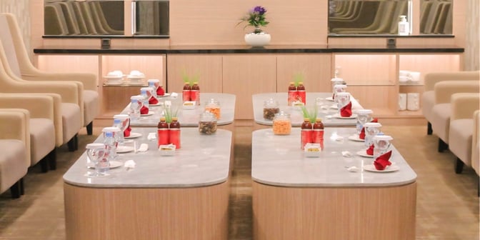The Concordia Lounge at Syamsudin Noor Airport features a seating area with tables set for refreshments, including bottled drinks and snacks.