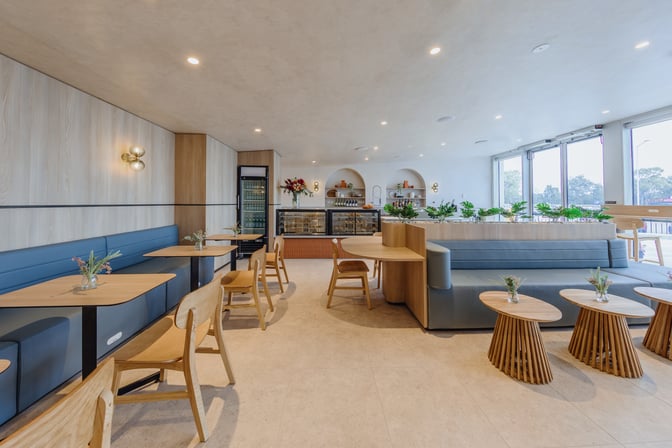The Plaza Premium Lounge at Sydney Airport features a seating area with tables and chairs, adjacent to a self-serve food station.