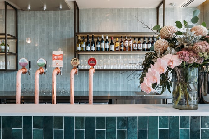 The bar at Plaza Premium Lounge in Sydney Airport offers a selection of draft beers and spirits with floral decor.