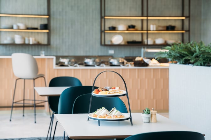 The Plaza Premium Lounge at Sydney Airport features a dining area with tiered plates of sandwiches and desserts on tables.