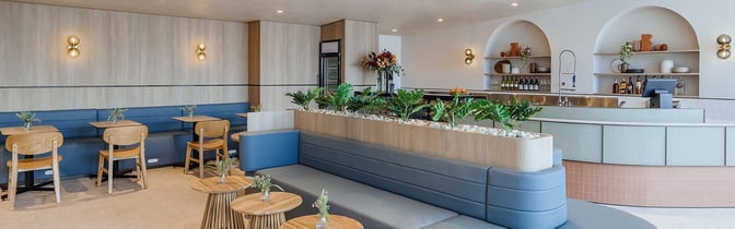 The Plaza Premium Lounge at Sydney Airport features a seating area with tables and chairs, adjacent to a bar with self-serve beverages.