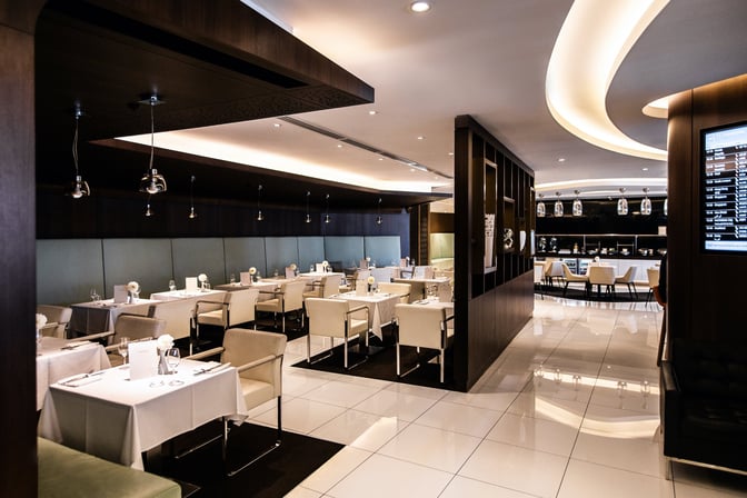 The dining area at The House lounge in Sydney Airport features table seating with white tablecloths and a view of the bar.
