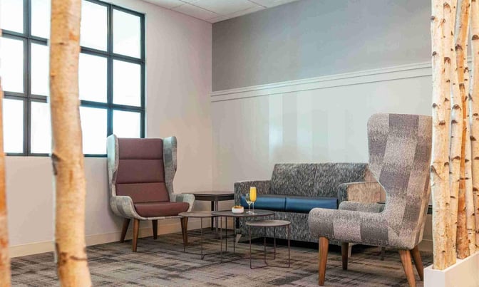 The seating area in the Escape Lounge at Syracuse Hancock International Airport features armchairs, a sofa, and a small table.