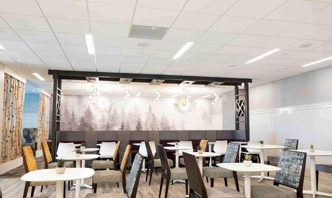The seating area in the Escape Lounge at Syracuse Hancock International Airport features tables and chairs with a forest-themed wall mural.