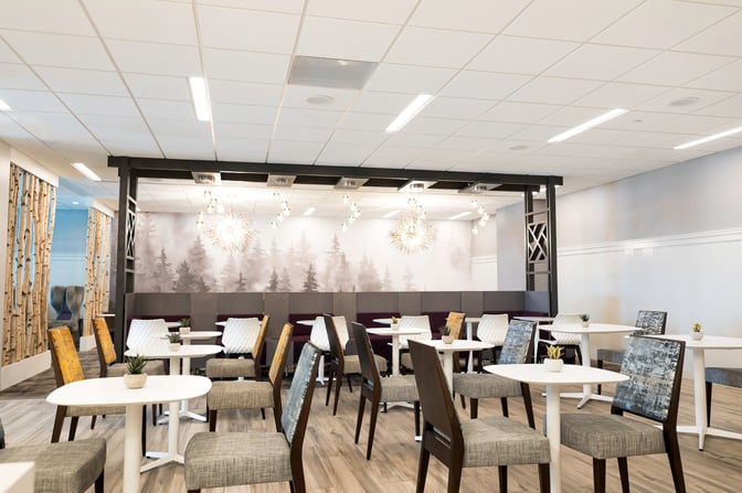 The seating area in the Escape Lounge at Syracuse Hancock International Airport features tables and chairs with decorative wall art.
