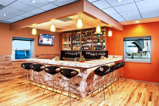 The Escape Lounge at Rhode Island T. F. Green Airport features a bar with high stools, offering a selection of spirits and wines.