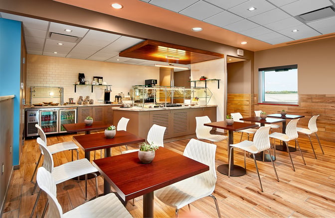 The dining area at Escape Lounge, Rhode Island T. F. Green Airport, features self-serve food stations and seating with airport views.