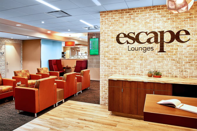 The seating area in the Escape Lounge at Rhode Island T. F. Green Airport features comfortable chairs and a visible flight information screen.