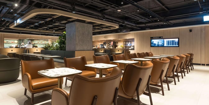 The Plaza Premium Lounge at Taipei Songshan Airport features a seating area with tables and chairs, adjacent to a service counter.