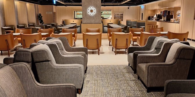 The Plaza Premium Lounge at Taipei Songshan Airport features a seating area with armchairs and tables, adjacent to a self-serve food station.