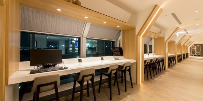 The Oriental Club Lounge at Taiwan Taoyuan International Airport features a row of workstations with computers and seating overlooking the airport.