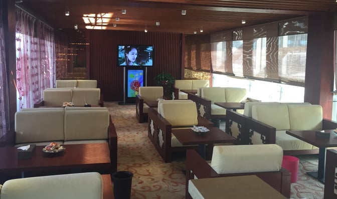 The seating area in Taiyuan Wusu International Airport's First Class Lounge features cushioned chairs and tables with a television for entertainment.