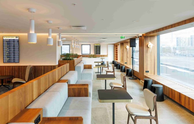 The Tallinn Airport LHV Lounge features booth seating with tables and chairs, offering views of the airport through large windows.