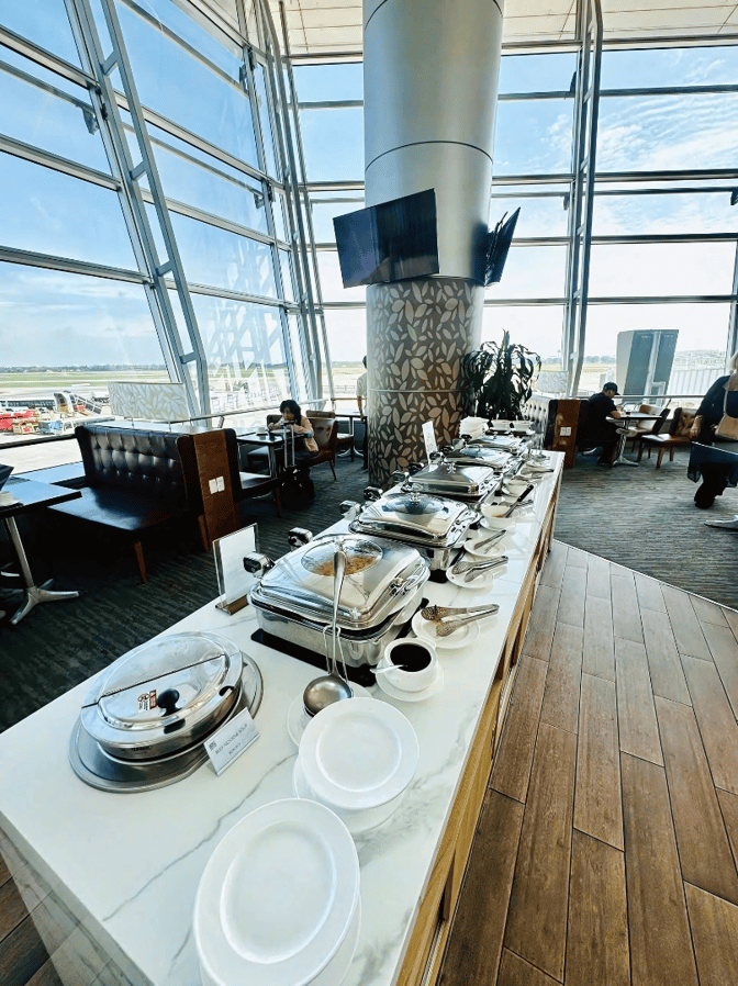 The Rose Business Lounge at Tan Son Nhat International Airport features a buffet area with self-serve hot dishes and seating with airfield views.