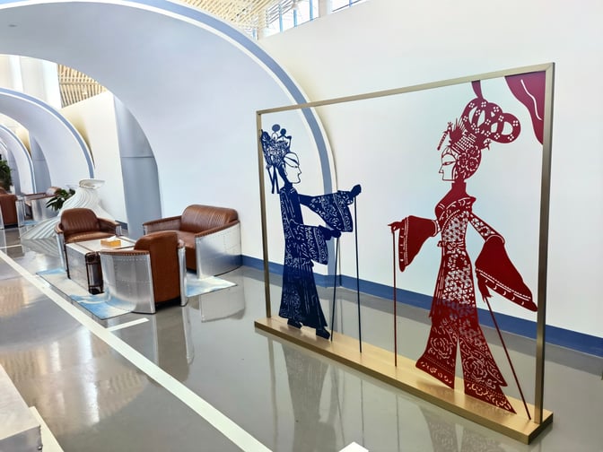Seating area in Tangshan Sannühe Airport's First Class Lounge features armchairs and decorative art panels for passenger relaxation.