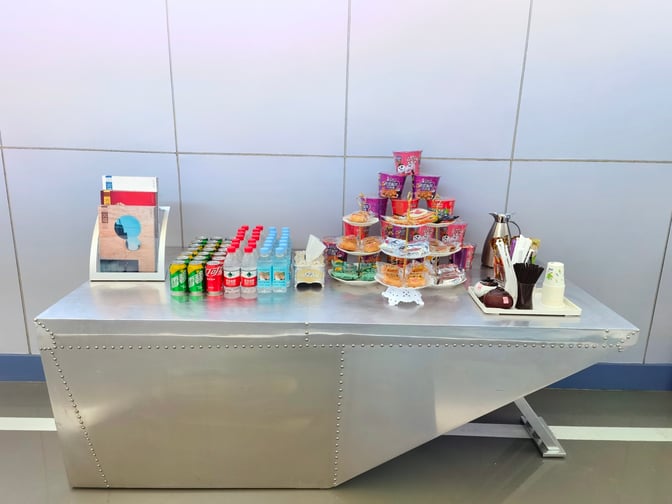 A refreshment station in the First Class Lounge at Tangshan Sannühe Airport offers snacks, beverages, and reading materials.