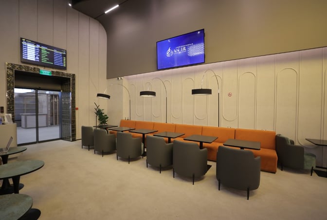 The Anjir Business Lounge at Tashkent International Airport features a seating area with tables, chairs, and a visible flight information screen.