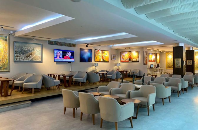 The seating area in the Primeclass CIP/VIP Lounge at Tbilisi International Airport features comfortable chairs and tables with wall-mounted televisions.