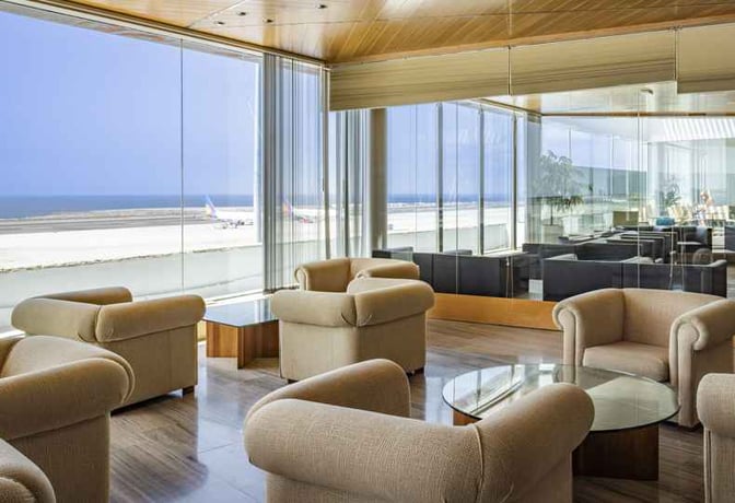 The seating area in Sala Montaña Roja at Tenerife South Airport offers armchairs and glass tables with views of the runway.