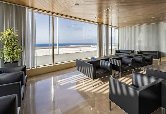 The seating area in Sala Montaña Roja at Tenerife South Airport offers comfortable chairs with expansive views of the runway and ocean.
