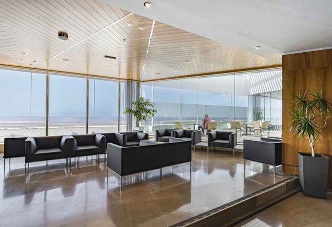 The Sala Montaña Roja lounge at Tenerife South Airport features seating areas with views of the runway through large windows.