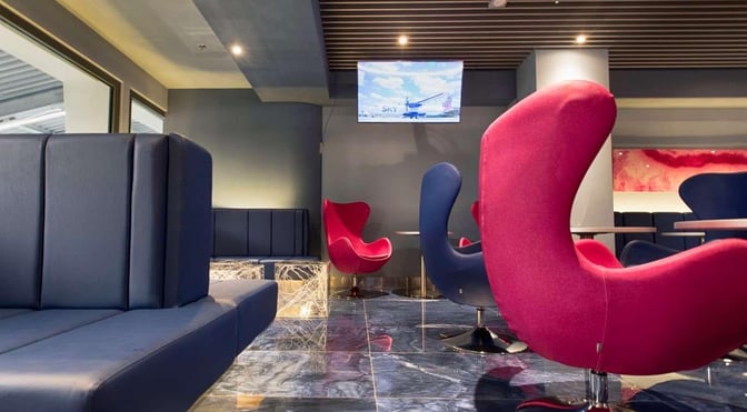 The seating area in Skyserv Manolis Andronikos Lounge features modern chairs and booth seating with a television for entertainment.