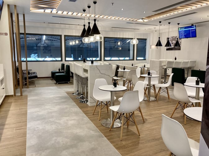 The Lounge Thessaloniki at Thessaloniki Makedonia International Airport features a seating area with tables and chairs, offering views of the tarmac.