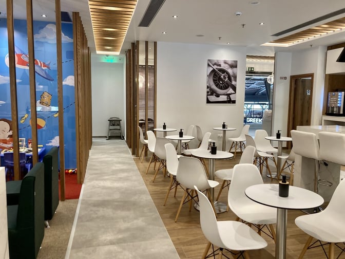 The Lounge Thessaloniki features a seating area with small tables and chairs, adjacent to a children's play section.