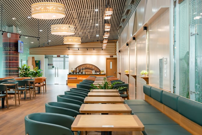 The SH Premium Lounge at Tho Xuan Airport features a seating area with tables and chairs, and a self-serve refreshment counter.