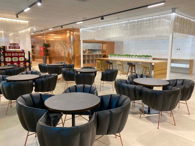 The Scanderbeg Lounge at Tirana International Airport features a seating area with round tables and cushioned chairs, adjacent to a bar counter.