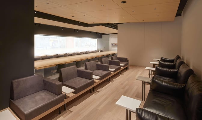 The seating area in POWER LOUNGE CENTRAL at Tokyo International Airport features individual chairs with side tables and a long communal counter.