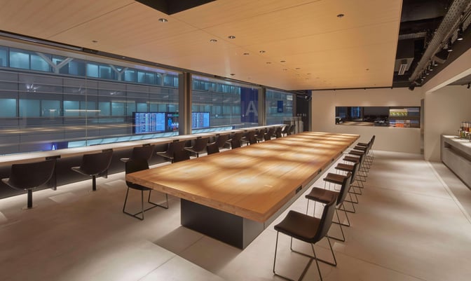 The POWER LOUNGE NORTH at Tokyo International Airport features a long communal table and counter seating with flight information displays.