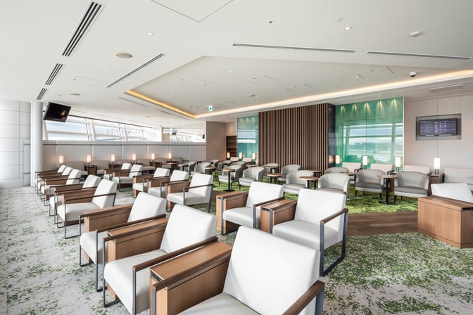 The TIAT Lounge at Tokyo International Airport features spacious seating with individual tables and a view of the airport runway.