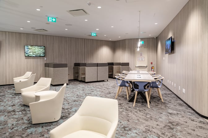 The Plaza Premium Lounge at Toronto Pearson features a seating area with individual chairs, a communal table, and wall-mounted televisions.