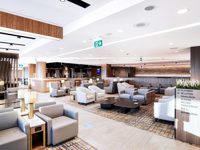 The Plaza Premium Lounge at Toronto Pearson International Airport features a spacious seating area with armchairs and tables, adjacent to a bar.