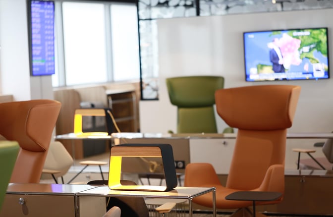 The seating area in La Croix Du Sud lounge at Toulouse Blagnac Airport features comfortable chairs, small tables, and a television screen.