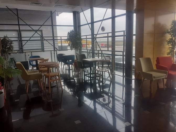 The Horizons Lounge at Traian Vuia International Airport features a seating area with tables and chairs overlooking the airport runway.