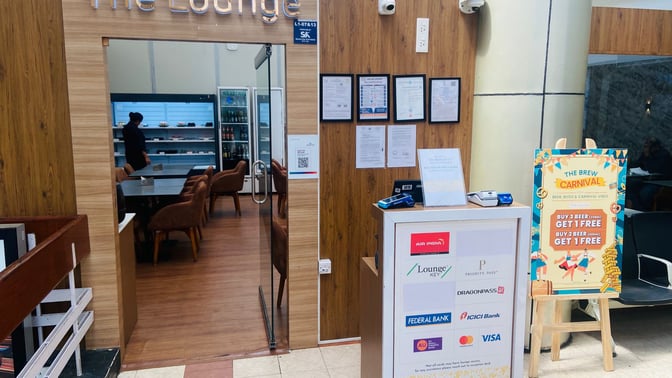 The entrance to The Lounge at Thiruvananthapuram International Airport features seating visible inside and promotional signage outside.