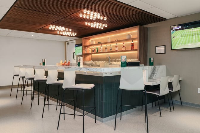 The bar at the Escape Lounge in Tulsa International Airport offers counter seating with a selection of spirits and a television.