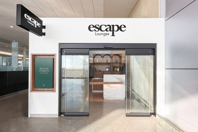 The entrance to the Escape Lounge at Tulsa International Airport features sliding glass doors and a reception desk inside.